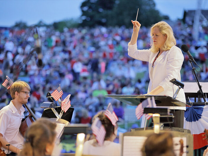 Elizabeth Schulze conducting at Antietam National Battlefield with patriotic decor on stage and crowds behind her.